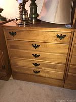 Photo of a honey-toned wood vintage cabinet with five drawers and ornate black metal handles, lamps placed on top.