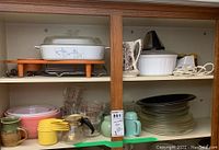 Shelf with vintage glass and ceramic kitchenware including Corning Ware lidded casserole, Pyrex pie plates, mixing bowls, creamers, measuring cups