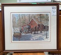 Full view of the framed artwork showing the winter farm scene with two horses, three men, and a red barn in the background, framed under glass in a wood frame.