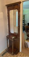 Full view of the oak hall stand showing beveled mirror, brass hooks, and umbrella holders.