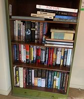Photo of a wooden bookshelf with multiple shelves fully stocked with assorted hardcover and paperback books including biographies and novels.