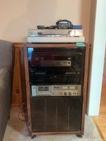 Photo of the stereo cabinet containing all electronics components, from top to bottom: turntable, CD player, cassette deck and FM receiver, with headphones on top.