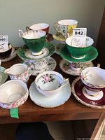 Tea cups and saucers arranged on table with cream and sugar bowls. Various floral and gold trim designs.