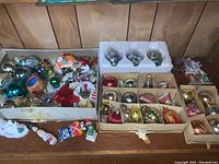Wide view of several boxes containing assorted vintage Christmas ornaments including glass balls, character figures, and bejeweled ornaments.