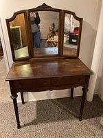Front view of antique dark wooden dressing table with attached three-panel mirror, two drawers, and turned legs.
