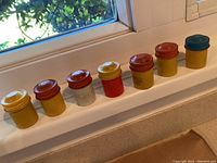 Seven Kodak metal film canisters in assorted colors lined up on a windowsill, showing variety of lid and body colors.