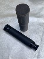Closed telescope next to black cylindrical case on white surface
