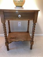 Front view of antique wooden table with spool-turned legs, drawer with white knob, and lower shelf.