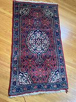 Full view of a small rectangular handwoven area rug with vibrant jewel tones and floral geometric patterns on a wooden floor.