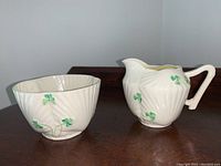 Front view showing both cream pitcher and sugar bowl with green shamrocks on cream porcelain with textured swirl pattern.