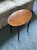 View of the small oval table showing the bookmatched wood veneer top with symmetrical grain pattern.