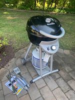 Front-left view of assembled Charbroil grill with propane tank below and grilling tools laid out on patio.