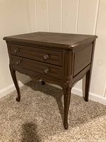 Side angled view of the brown wood French Provincial style side table with two drawers, showing carved legs and drawer fronts.