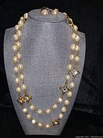 Full view of the long pearl necklace doubled with matching pearl earrings on grey jewelry display bust.