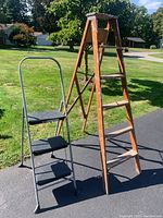 Photo showing both ladders in an outdoor setting: a wooden step ladder and a gray metal indoor step ladder with black Safety+ textured steps.