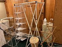 Overview of white metal drying rack, plastic hanging shelf organizer, woven hamper, and vintage wooden rack in corner.