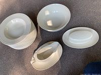 12 matching soup bowls stacked, large serving bowl, gravy boat with base, butter dish with lid all visible