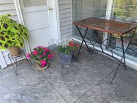 Wide shot showing copper top plant table, three ceramic plant pots with annual plants, and a small black metal chair plant stand with plant.