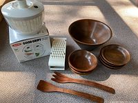 Full view of all items including large wooden bowl, six smaller bowls, two wooden servers, white salad spinner in box, and white handheld grater.