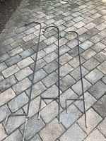 Three black metal shepherd's hooks laid on patterned stone pavement, showing full length and bases