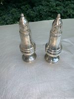 Pair of weighted sterling silver salt and pepper shakers marked Preisner Sterling, standing upright on a white textured surface with outdoor background.