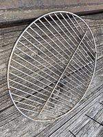 Oval metal grill rack with crossbars, angled on a wooden surface showing the grill rack structure.