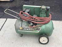 Side view of green Speedaire air compressor showing tank, wheels, handle and motor with hose wrapped around.
