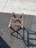Front view of the worn wooden blanket holder lying flat on asphalt showing the fabric straps and wooden frame.
