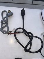 Two electrical appliance power cords laid flat on a white surface. One black cord with a three-prong plug and one gray cord with molded three-prong plug, both with exposed wiring.