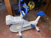 Full view of Monark exercise bike showing white frame, blue handlebars, blue pedals and seat.