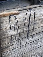 Two black folding metal stands placed upright side by side on a wooden surface outdoors.
