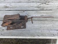 Side view of portable scissor car jack displaying rust and a foldable crank handle lying horizontally on a wooden surface.