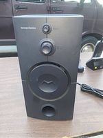 Front view of the Harman Kardon powered subwoofer showing controls, speaker driver, and bass reflex port.