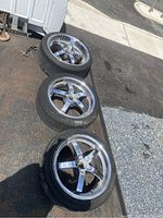 Photo showing three used 18-inch rims with tires placed on the ground outdoors, rims have five-spoke design and tires attached.