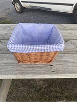 Front view of small rectangular woven wooden basket with blue and white checkered cloth liner on weathered wooden surface.