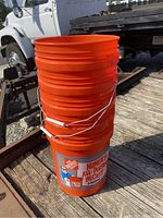 Stacked orange plastic Home Depot buckets with metal handles outdoors on wooden surface.