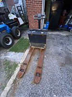 View showing rusted forks and battery compartment of the Toyota electric pallet jack on asphalt ground.