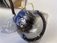 Photo of vintage headphones sealed in plastic wrap, showing padded black ear cups and coil cord.