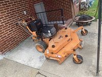 Front left angle showing orange steel deck, SCAG logo on deck and engine cover, caster front wheels and rear traction wheels