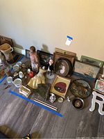 Wide view of the lot showing all antique dolls, tea cups, decorative items and framed artworks laid on floor.