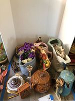 Wide view of assorted antique home decor items including pottery, tins, figurines, and decorative flowers on a surface.