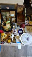 Full view of the lot showing framed pictures, plates, ceramic bird-shaped creamer, glass oil lamp, and assorted small items.