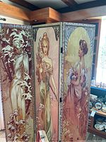 Full front view of three-panel folding screen showing snow-covered winter panel on left, flower-holding figure on center panel and floral-backed figure on right.