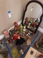 Overview photo showing multiple ceramic Asian figurines, small antiques including a wall mirror and various decorative items, arranged on the floor inside blue tape boundaries.