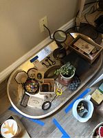 Full view of large silver serving tray with contents including daguerreotype photographs, decorative boxes, buttons, pocket tools, hand mirror, and artificial grape clusters arranged inside.