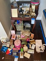 Overall assortment of miniature perfume bottles, powders, lipstick display cases, and collectible items on and around a small table.