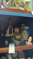View showing trophies, vintage glass jars with lids, a ceramic bird figurine, small wrapped item, and boxes including an ornate metal jewelry box and a striped tin container.