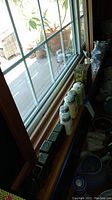 View of the lot placed on a window sill showing various salt and pepper shakers, glass bottles, and a tin box