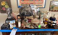 Overview of lot showing multiple vintage items on table including pillbox hat, perfume bottles, and bust award.