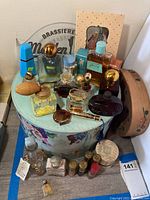 Wide view of assorted vintage perfume bottles, several gold capped and shaped uniquely, with two decorative round storage boxes